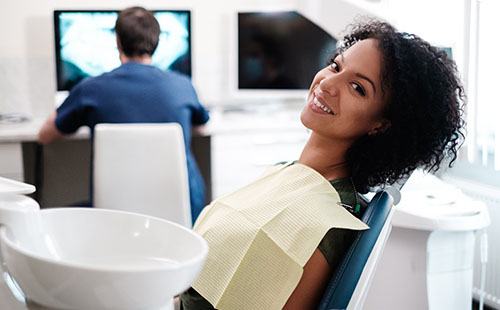 A young woman smiling while her dentist examines her dental X-rays during a checkup and teeth cleaning in Delafield