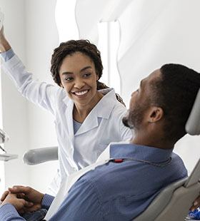 A female dentist adjusts the overhead light in preparation for performing a dental checkup on a male patient