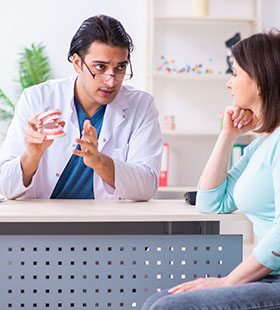 A dentist holds a mouth mold and explains to a female patient why regular checkups and cleanings are important