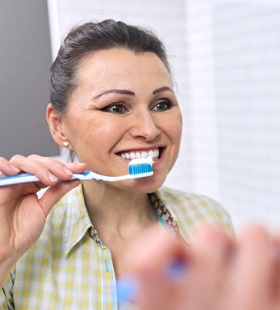 A middle-aged woman standing in front of her bathroom mirror preparing to brush her teeth