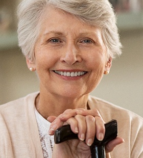 An older woman holding onto her cane while showcasing her restored smile thanks to dental implants