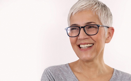 An older woman wearing glasses and smiling after receiving her dental implants in Delafield