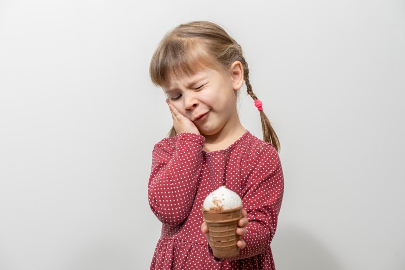 little girl with ice cream holding her cheek in pain